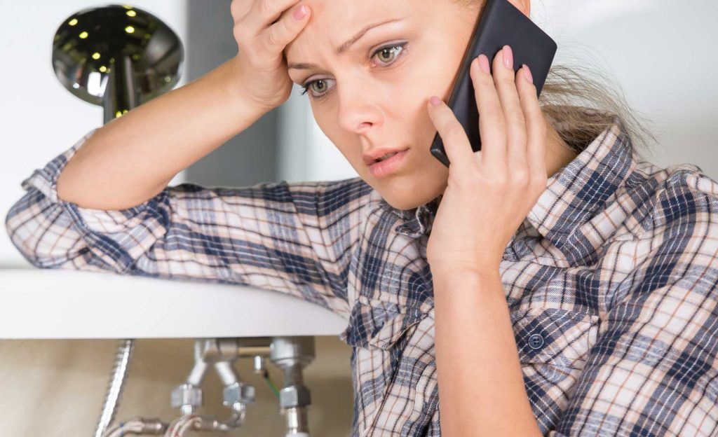 Distressed woman making phone call over water pipes