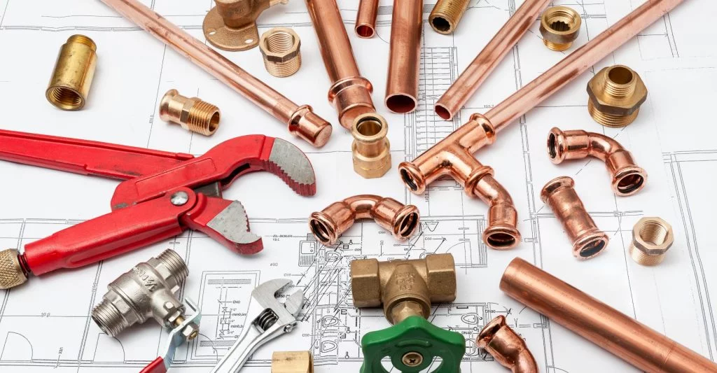 Plumbing parts and plumber tools laid over housing plans